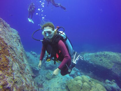 diver wearing bcd swimming over rocks
